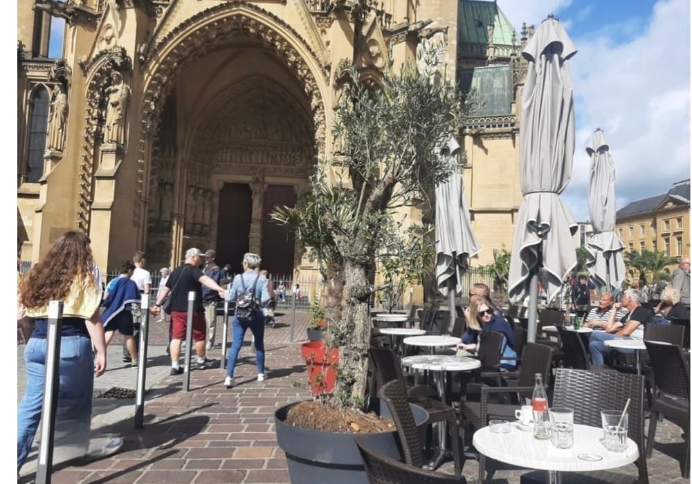 Ambiance animée sur une terrasse de café à Metz, avec des passants et des terrasses ensoleillées