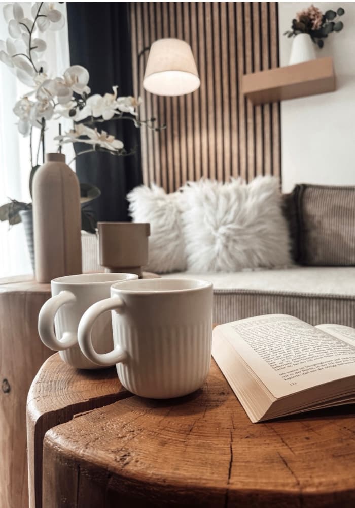 Tasses et livre sur la table du salon avec coussins en fourrure en arrière-plan pour un séjour à Metz