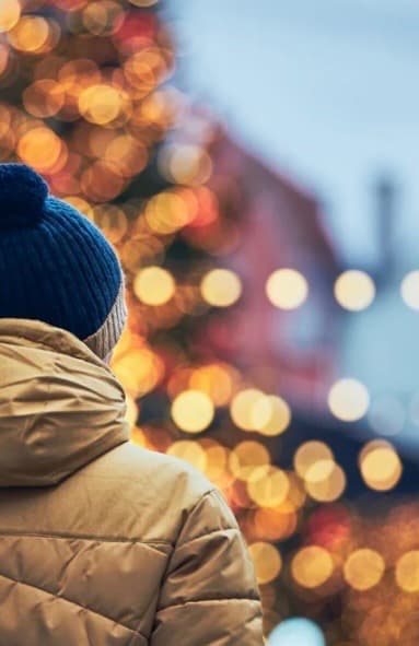 Personne de dos avec un bonnet bleu devant le flou lumineux doré d'un sapin de Noël.