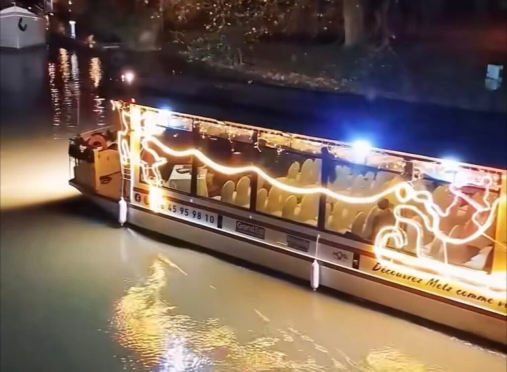 Bateau de promenade illuminé de motifs de Noël naviguant de nuit sur la Moselle à Metz.