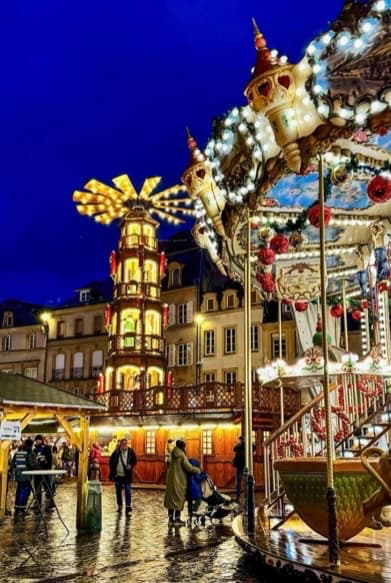 Pyramide de Noël en bois lumineuse et chalets illuminés sur un marché de Noël de nuit avec des visiteurs