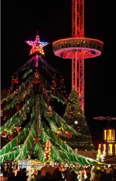 Grand sapin de Noël illuminé surmonté d'une étoile devant la City Skyliner (tour panoramique) éclairée en rouge à Metz